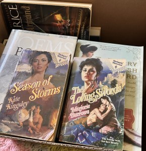 Box of Books with poetry, Ann Rice, and two worn out paperbacks on top that are both Harlequin historical romance books.